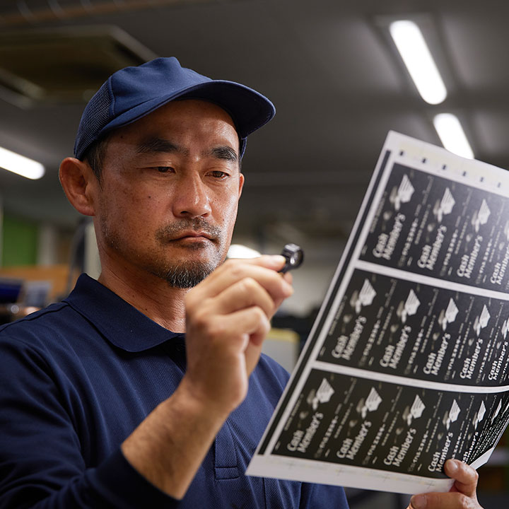 ルーペで印刷の仕上がりを確認するスタッフ